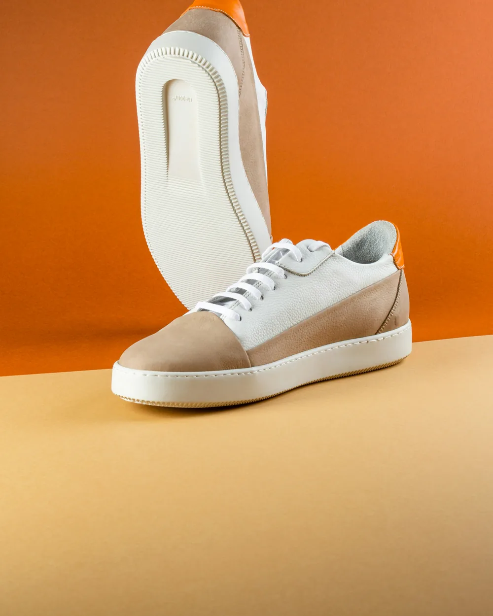 A suede and leather sneaker on an orange backdrop