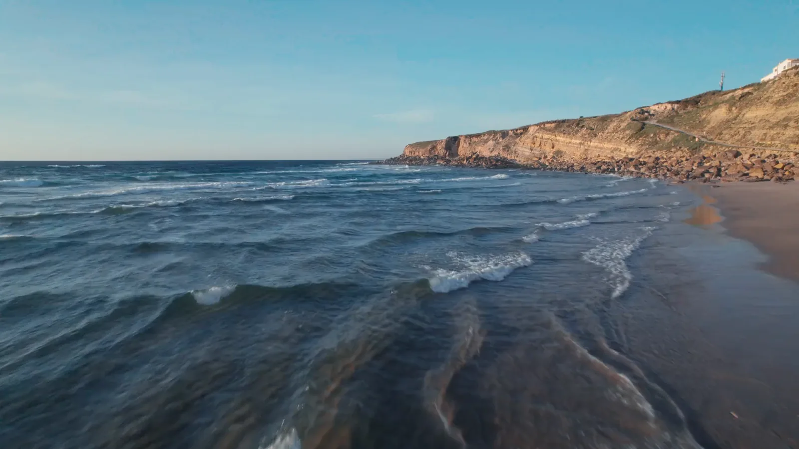 Waves rolling in toward a line of sea cliffs on a bright afternoon